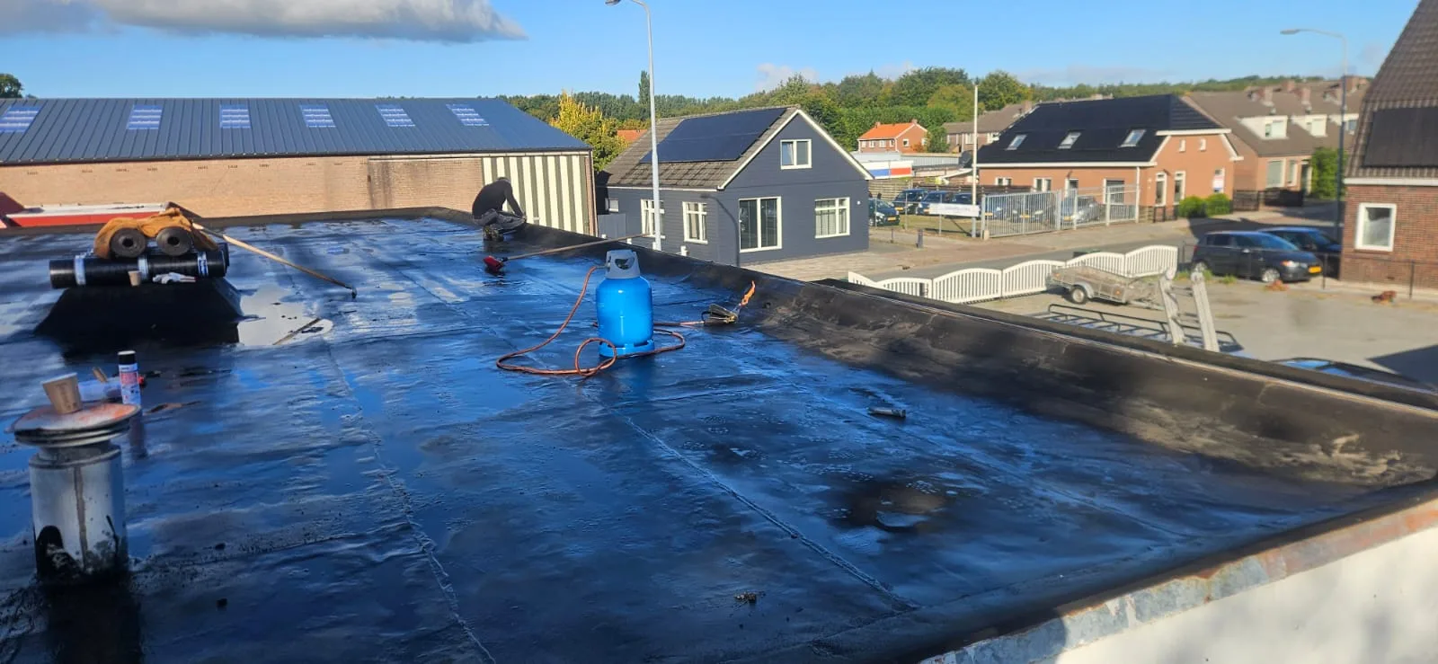 Chantier en cours sur un grand toit plat résidentiel : membrane bitumineuse fraîchement soudée (surface noire brillante),…
